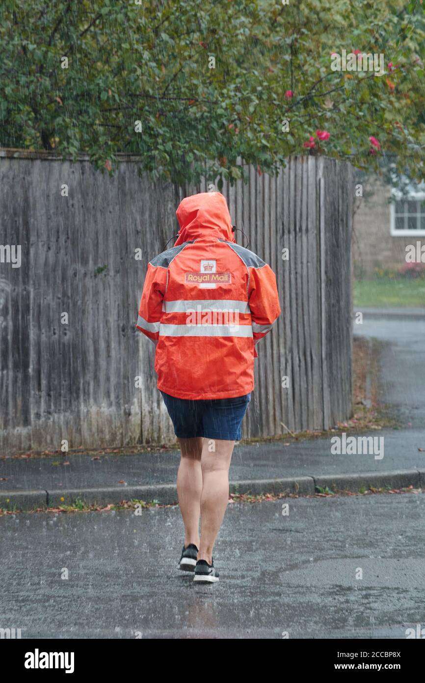 Postwoman du Royal Mail effectuant une livraison le jour d'été pendant la pluie battante. Banque D'Images