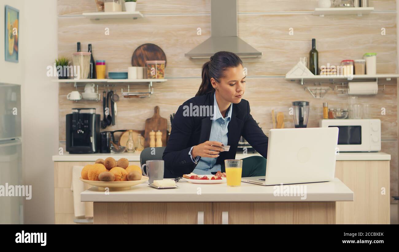 Femme d'affaires effectuant le paiement en ligne par carte de crédit sur un ordinateur portable pendant le petit déjeuner. Acheter en ligne des biens et des vêtements, en utilisant la technologie moderne dans la vie quotidienne, faire des paiements par Internet Banque D'Images