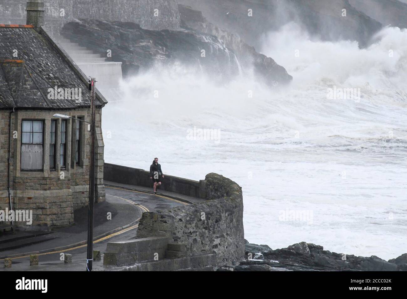 Porthleven, Cornwall, Royaume-Uni. 21 août 2020. Météo Royaume-Uni. D'énormes vagues de la tempête Ellen fracassent dans les falaises et les défenses côtières à Porthleven, dans les Cornouailles, au début de la matinée à marée haute, lors d'une journée de vents de force gale. Un piéton marche le long d'une route sur le front de mer. Crédit photo : Graham Hunt/Alamy Live News Banque D'Images