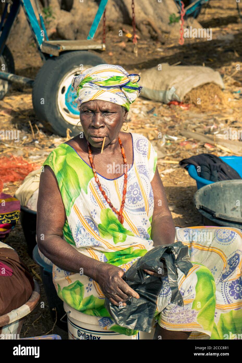 Femme sur le marché assise sur un conteneur en plastique attendant des clients au Sénégal, Afrique - Photographie: Iris de Reus Banque D'Images