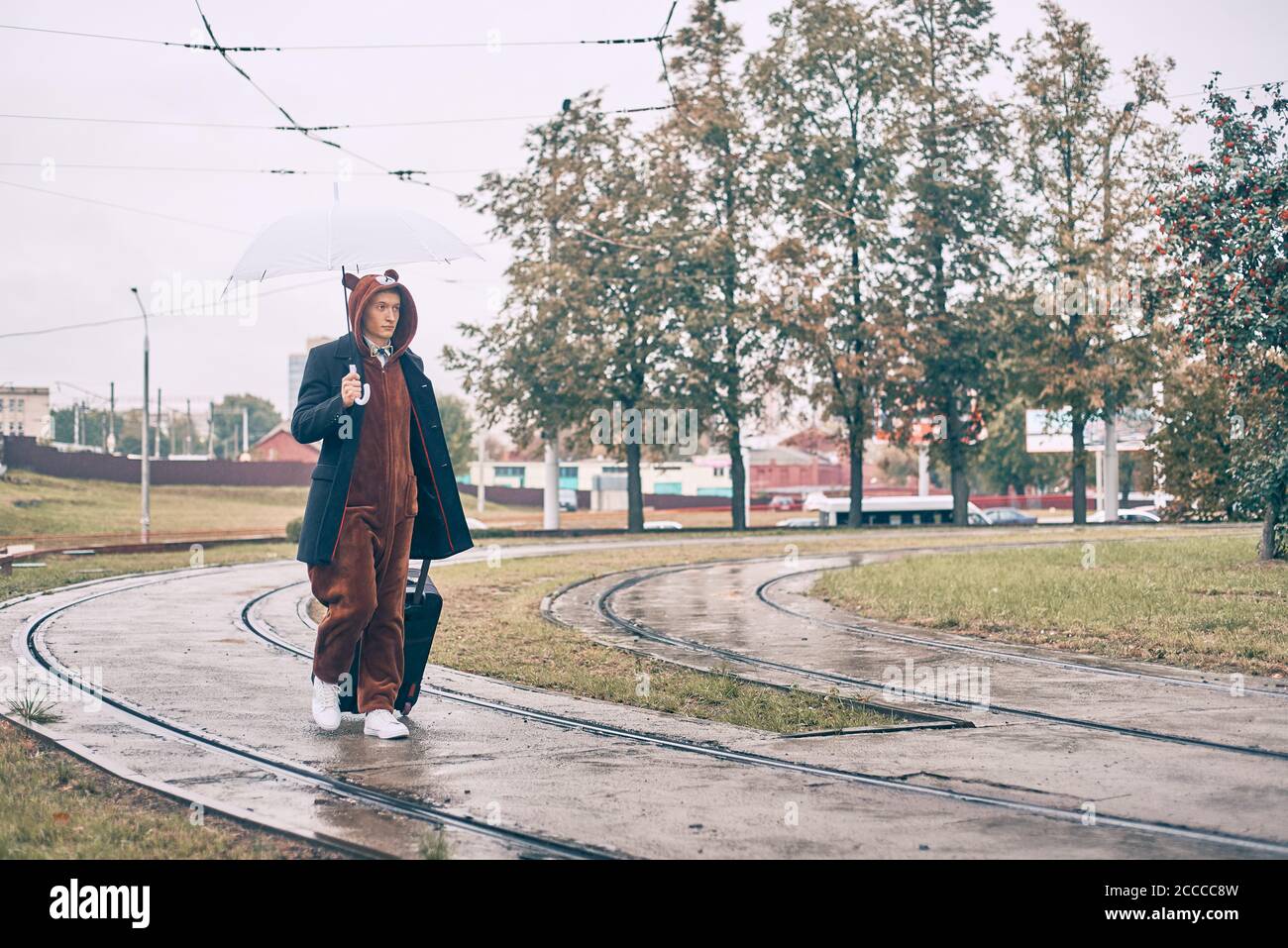 l'homme avec une valise marche le long de la route. guy tient un parapluie sous la pluie Banque D'Images