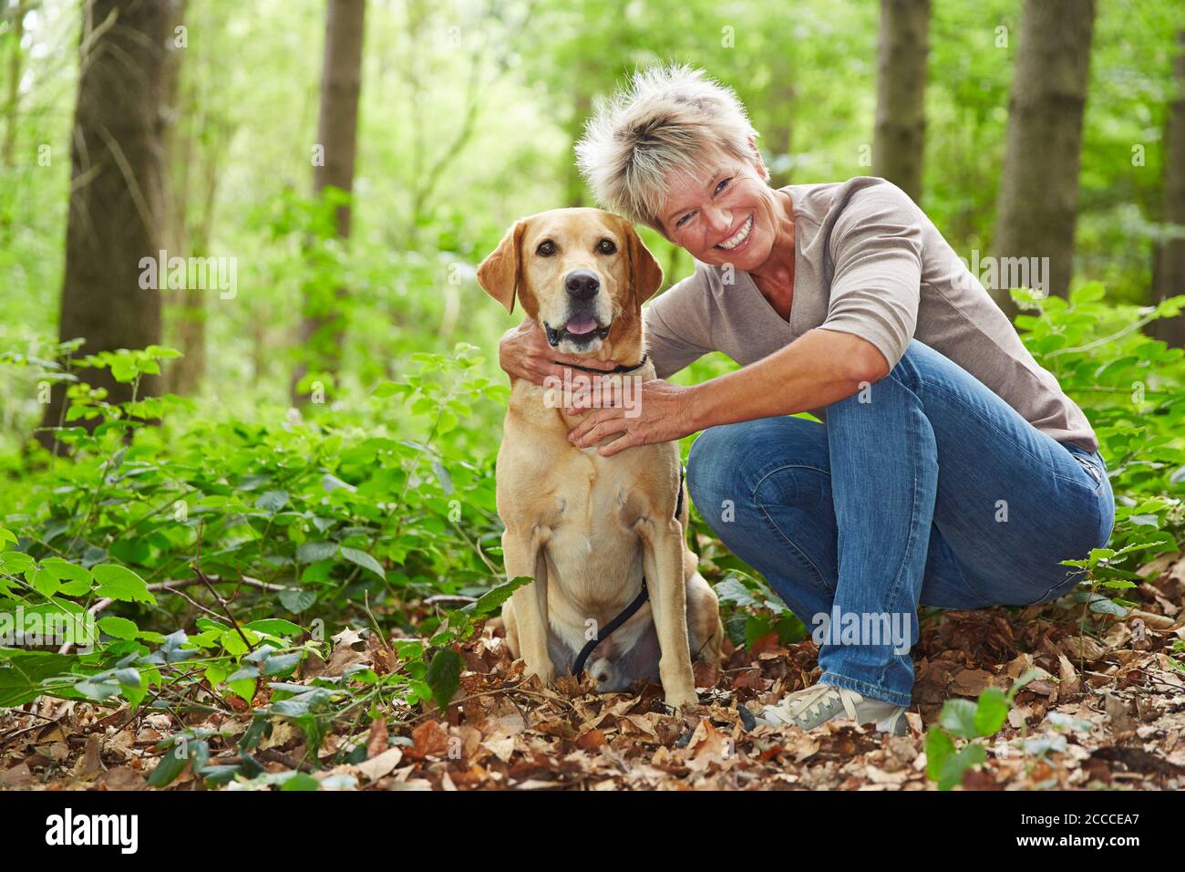 Femme âgée souriante avec son chien Labrador Retriever dans le forêt Banque D'Images