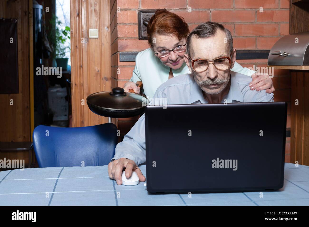 Problèmes familiaux dus à l'ordinateur. Un couple âgé dans la cuisine, un homme âgé utilise un ordinateur portable Banque D'Images