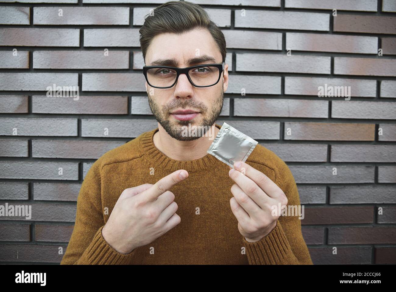 Un jeune homme au look attrayant tient le préservatif. Banque D'Images