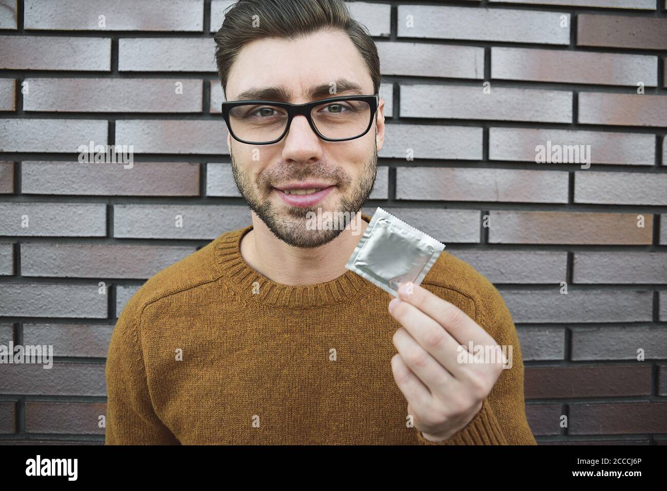 Un jeune homme au look attrayant tient le préservatif. Banque D'Images