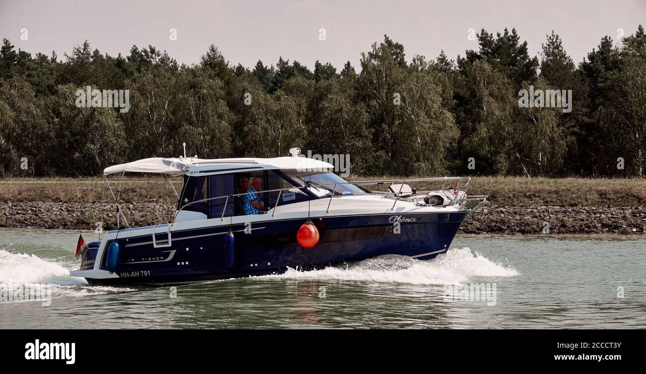 Gifhorn, Allemagne, le 9 août 2020: Bateau à moteur bleu foncé avec toit blanc se déplace à grande vitesse à travers le canal avec des éclaboussures d'eau Banque D'Images