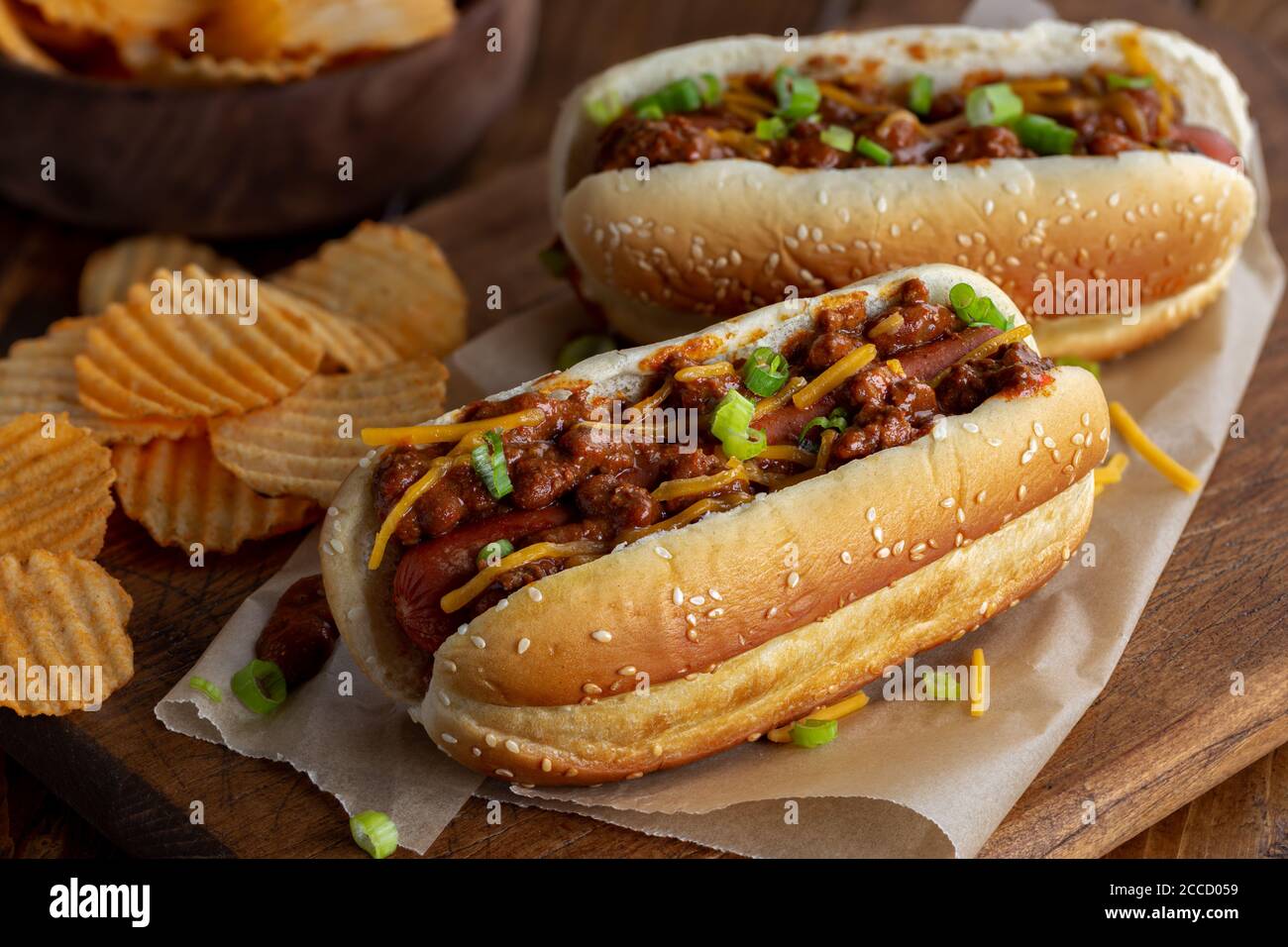 Chien chaud au Chili avec cheddar et oignons verts un pain de graines de sésame avec des chips de pomme de terre sur un rustique planche en bois Banque D'Images