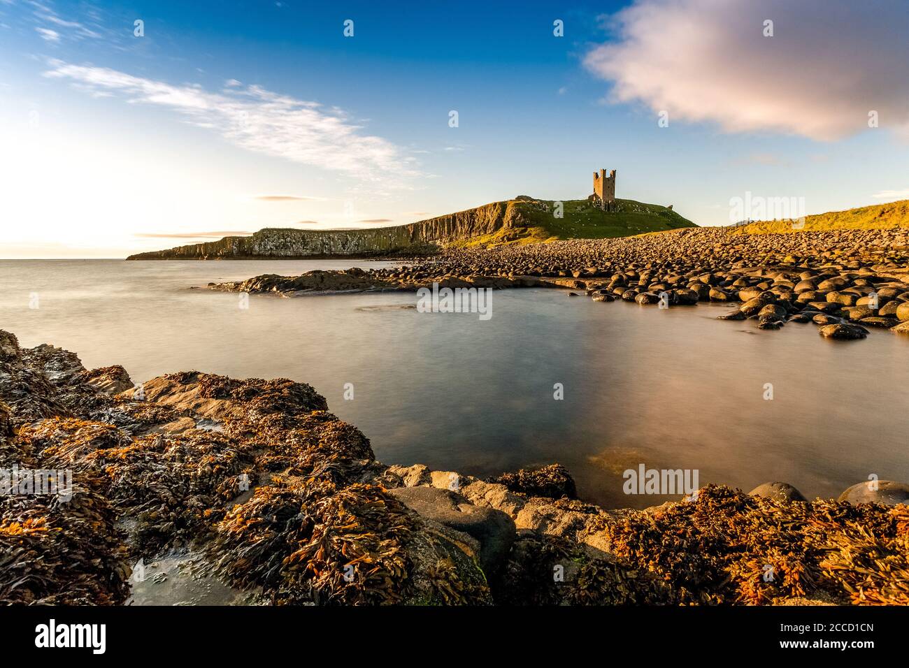 Le château de Dunstanburgh a tourné tôt le matin avec la mer du Nord qui s'est abatée dans la baie. Banque D'Images