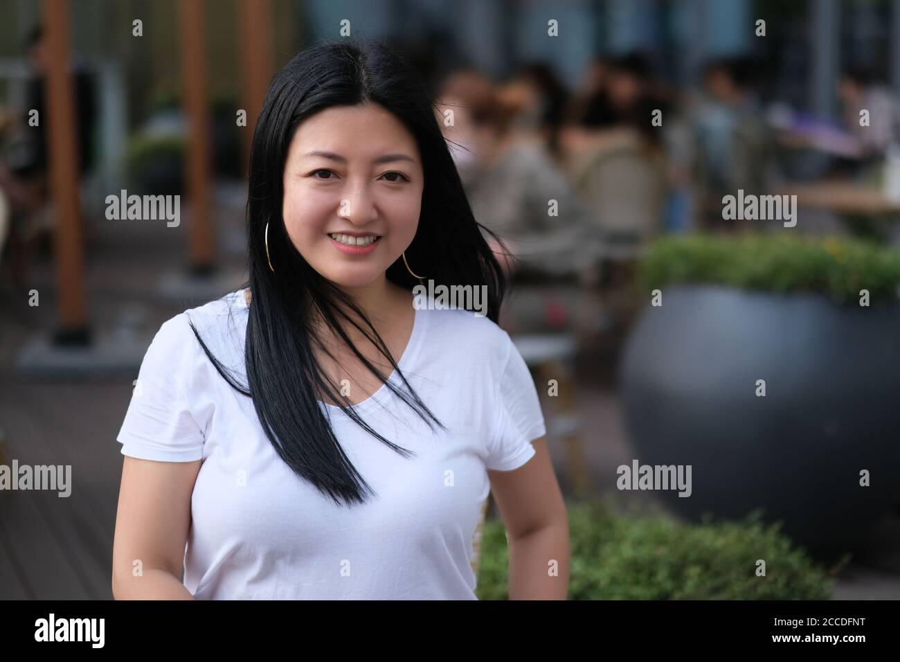 Une femme asiatique souriant et regardant l'appareil photo au café-terrasse. Arrière-plan flou Banque D'Images