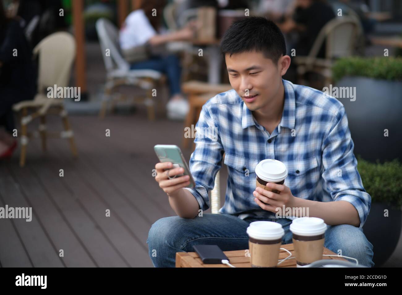 Moyen : un jeune homme asiatique utilisant un téléphone dans un café extérieur. Arrière-plan flou Banque D'Images