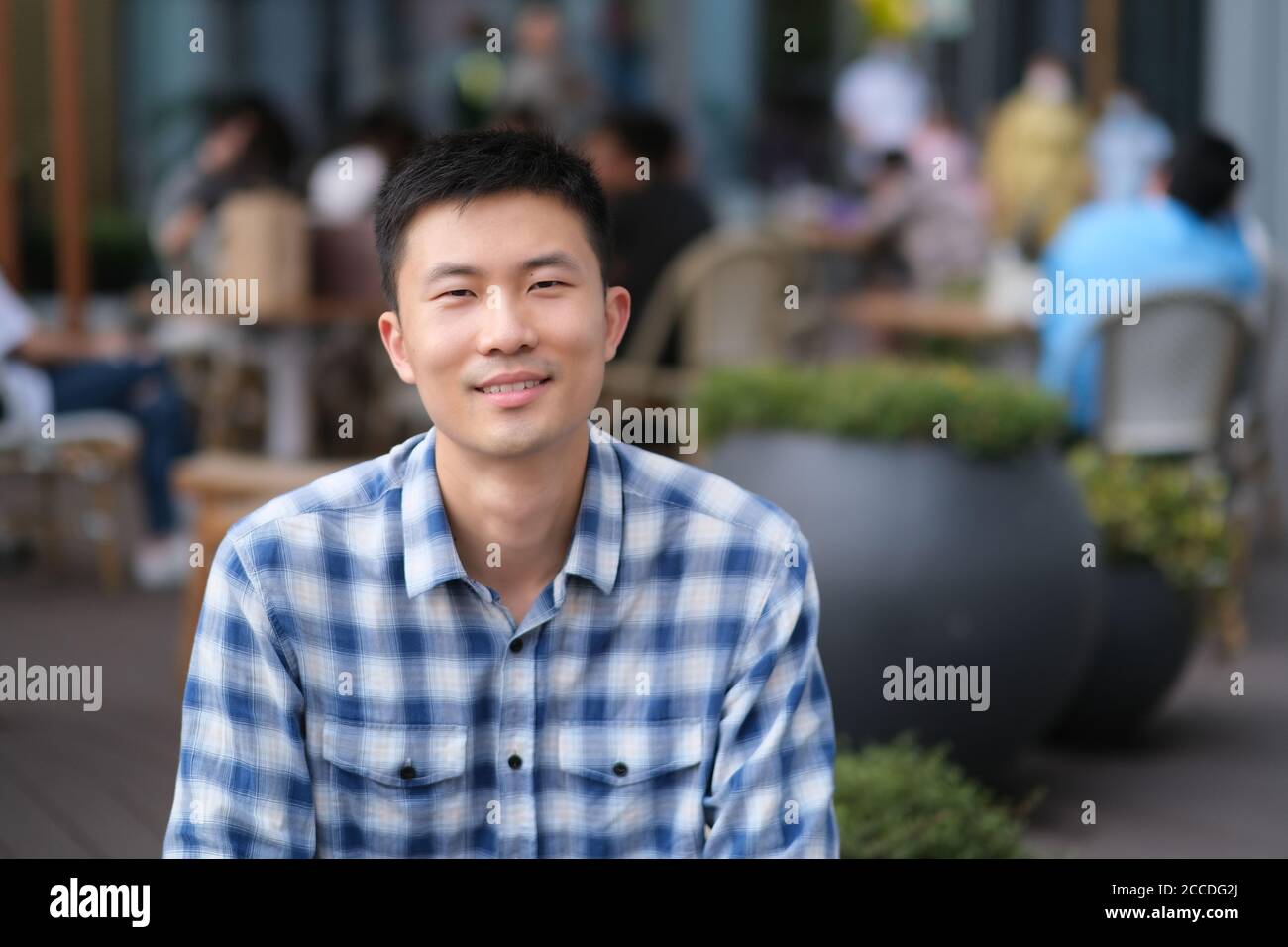 Portrait d'un jeune homme asiatique en chemise décontractée au café en plein air, souriant et regardant l'appareil photo. Arrière-plan flou Banque D'Images