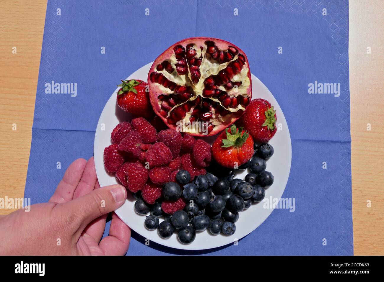 Gros plan d'une portion à la main ou d'une assiette ou d'un bol avec des bleuets, des framboises, des fraises et un demi-grenade Banque D'Images