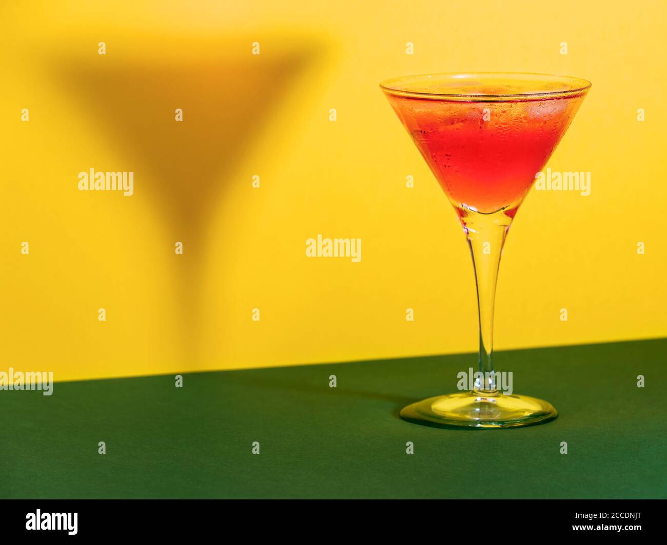 Cocktail rouge dans un verre façonnant son ombre sur un arrière-plan vert et jaune Banque D'Images