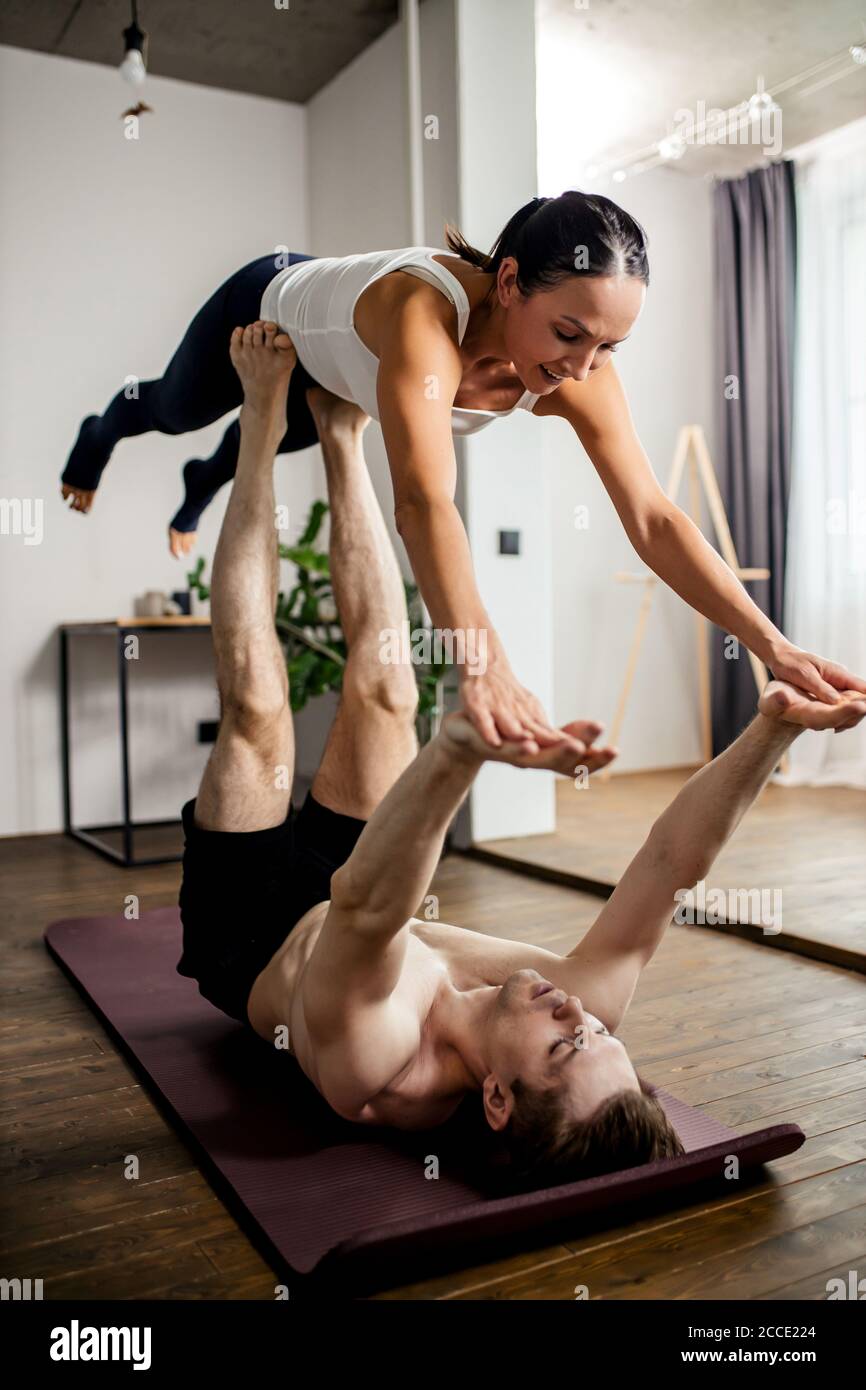 couple caucasien faisant des exercices de yoga à la maison, homme fort puissant tenir la femme sur ses jambes, heureux passant du temps à la maison, sur le sol Banque D'Images