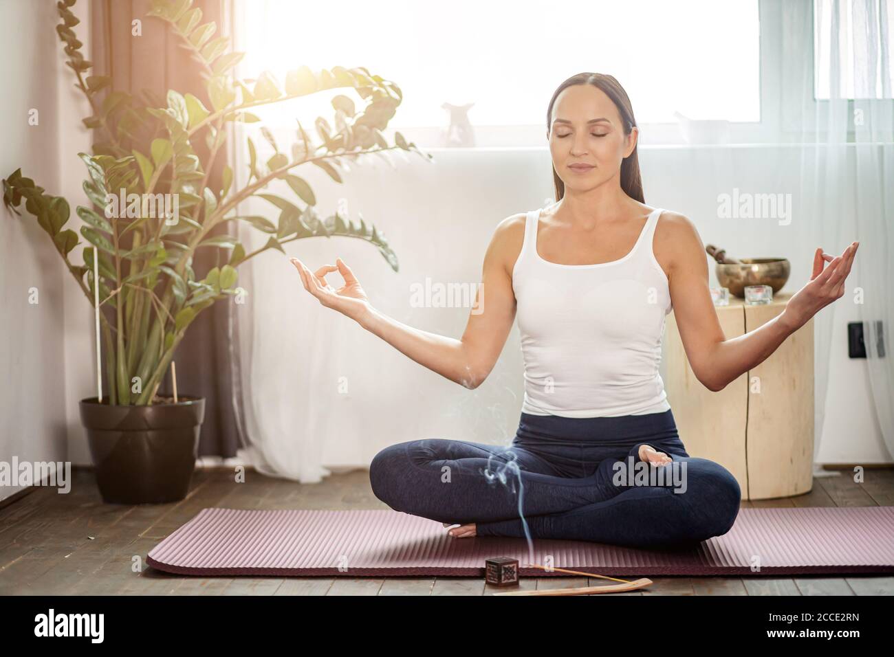 calme yogi femelle s'asseoir sur le sol dans la pose de lotus, méditer à la maison pendant la quarantaine, chaque matin commence du yoga, elle utilise des bâtons d'arôme Banque D'Images