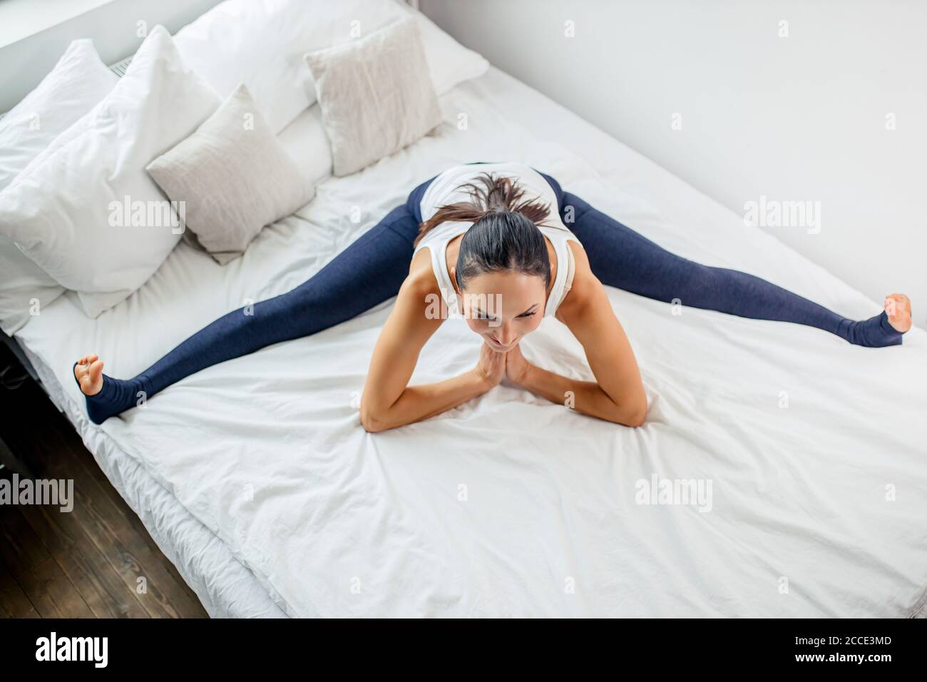 jeune femme yogi caucasienne s'asseoir dans une ficelle sur le lit à la  maison, la femme pratique, faire des exercices sur le lit, étirant les  jambes, dans des leggings Photo Stock -