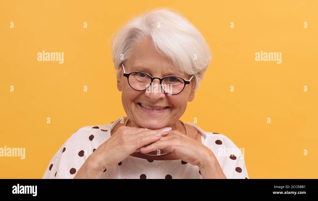 Femme âgée se reposant la tête sur ses mains et souriant. Isolé sur fond orange. Photo de haute qualité Banque D'Images