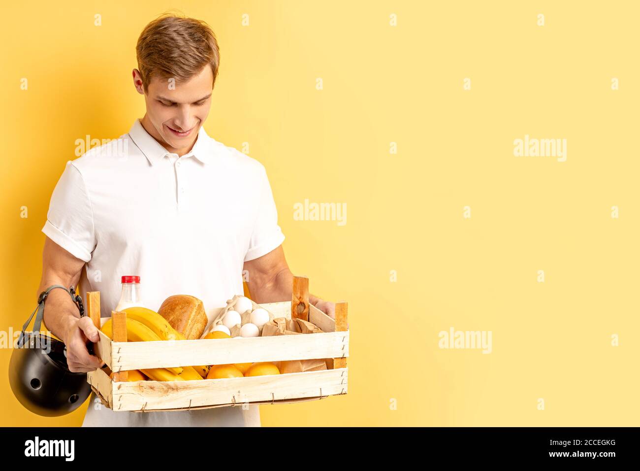livraison express par jeune homme vigoureux souriant en t-shirt blanc isolé sur fond jaune. messagerie, concept de service de livraison Banque D'Images