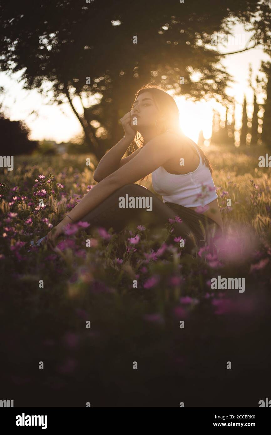 Adolescent ennuyeux assis dans le champ parmi les fleurs au coucher du soleil Banque D'Images