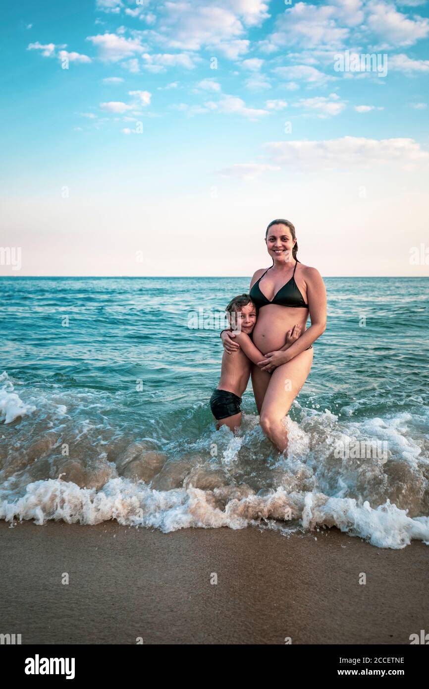 enfant de 5 ans embrassant la mère enceinte, genou profondément dans l'océan Banque D'Images