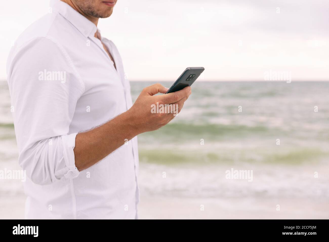 Téléphone homme d'affaires main tenant le smartphone SMS message en ligne à l'aide de l'application. Homme d'affaires sur la plage données de téléphone portable sur les vacances de voyage Banque D'Images