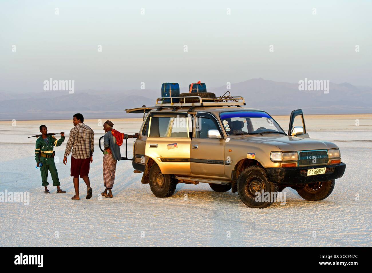 Guide, chauffeur et garde de sécurité locaux se tiennent à côté d'un véhicule à quatre roues motrices d'une compagnie touristique locale sur la croûte de sel de l'Assale Salt Lake, Banque D'Images