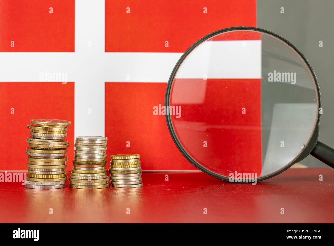 Loupe et pièces en face du drapeau du Danemark, concept d'économie de pays Banque D'Images