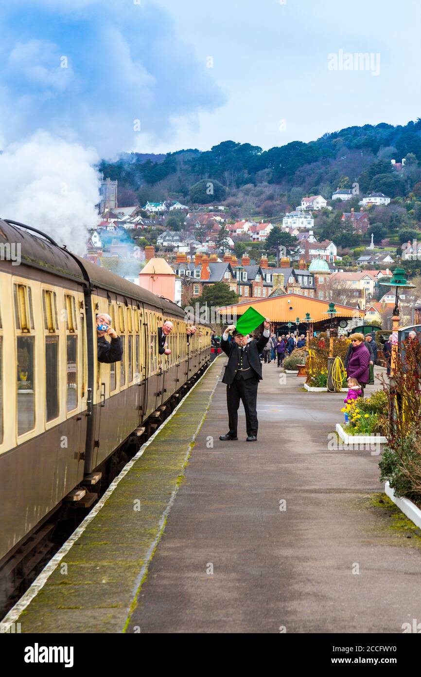 Un garde agite le drapeau vert pour autoriser un train à vapeur à partir de la gare de Minehead, West Somerset Railway Spring Gala event, Angleterre, Royaume-Uni Banque D'Images