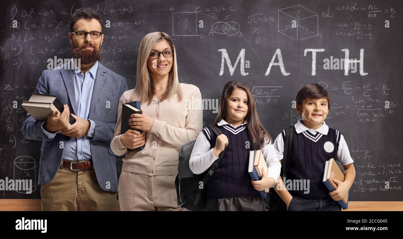 Professeurs de mathématiques, hommes et femmes, avec une écolière et un écolier devant un tableau noir avec du texte et des formules Banque D'Images