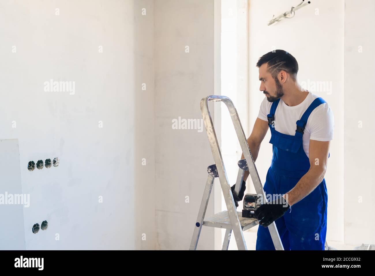 Le constructeur a mis le niveau laser sur l'échelle et regarde les marques sur le mur Banque D'Images