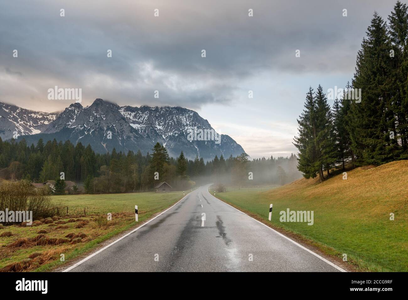 Tôt le matin sur la route de campagne à Schmalensee près de Mittenwald, la route est mouillée par la pluie, le brouillard léger s'élève et les tours de Karwendel dans le backgroun Banque D'Images