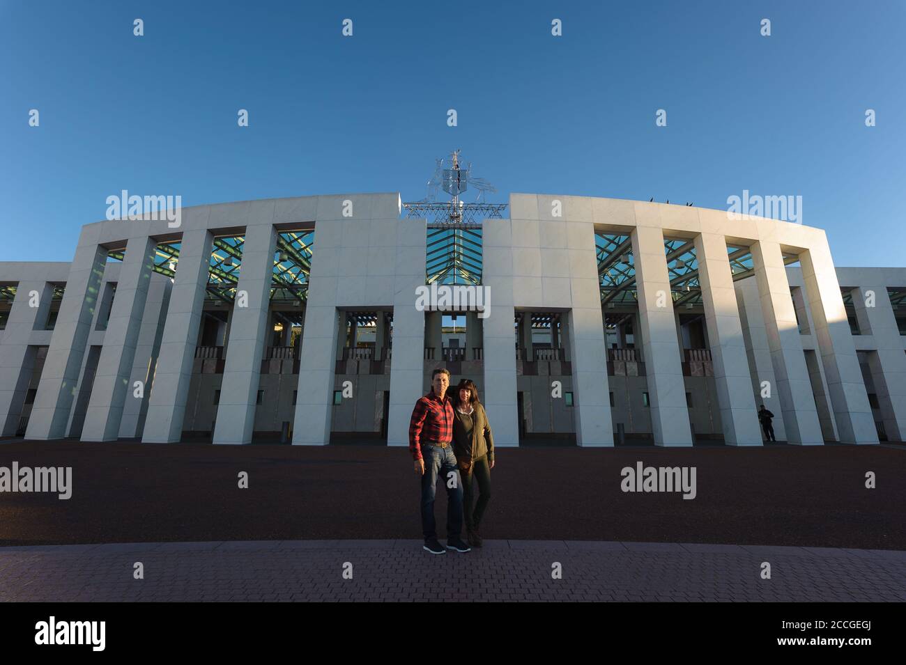 Un couple de touristes se tenant les uns les autres lors d'une journée d'hiver claire devant l'entrée principale du Parlement australien à Canberra. Banque D'Images