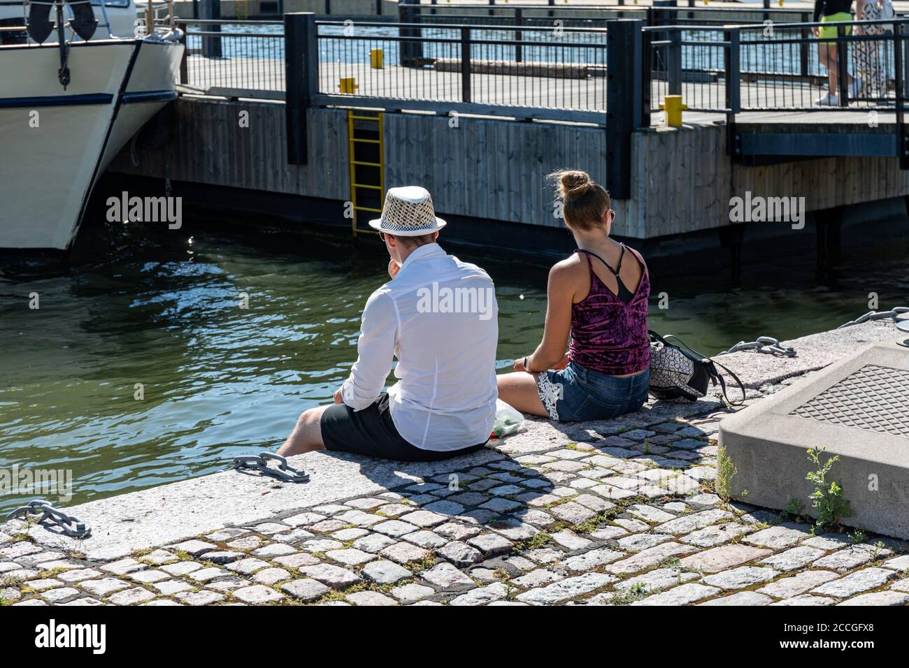 Jeune couple en vêtements d'été assis sur un quai à Helsinki, en Finlande Banque D'Images