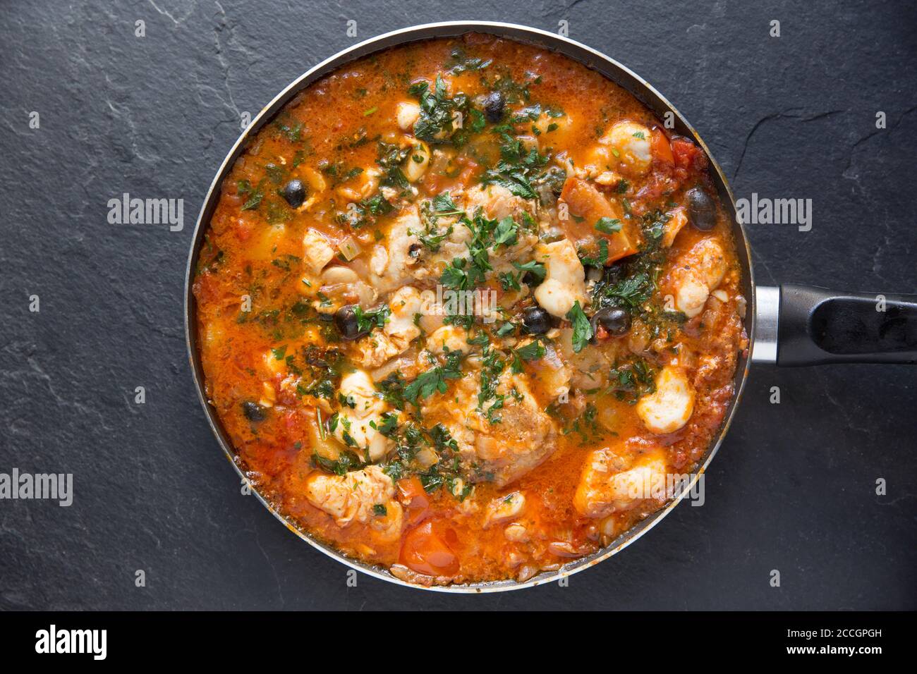 Un ragoût de poisson fait maison avec des joues de monkfish et des joues de rayon cuites dans une sauce tomate avec des pommes de terre bouillies, des olives noires et garnies de Banque D'Images