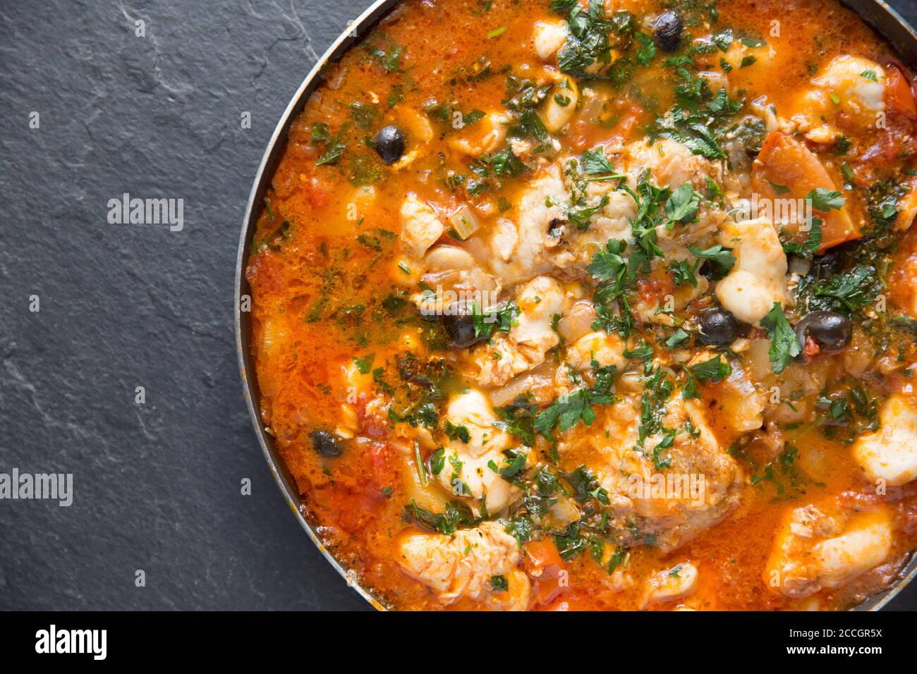 Un ragoût de poisson fait maison avec des joues de monkfish et des joues de rayon cuites dans une sauce tomate avec des pommes de terre bouillies, des olives noires et garnies de Banque D'Images