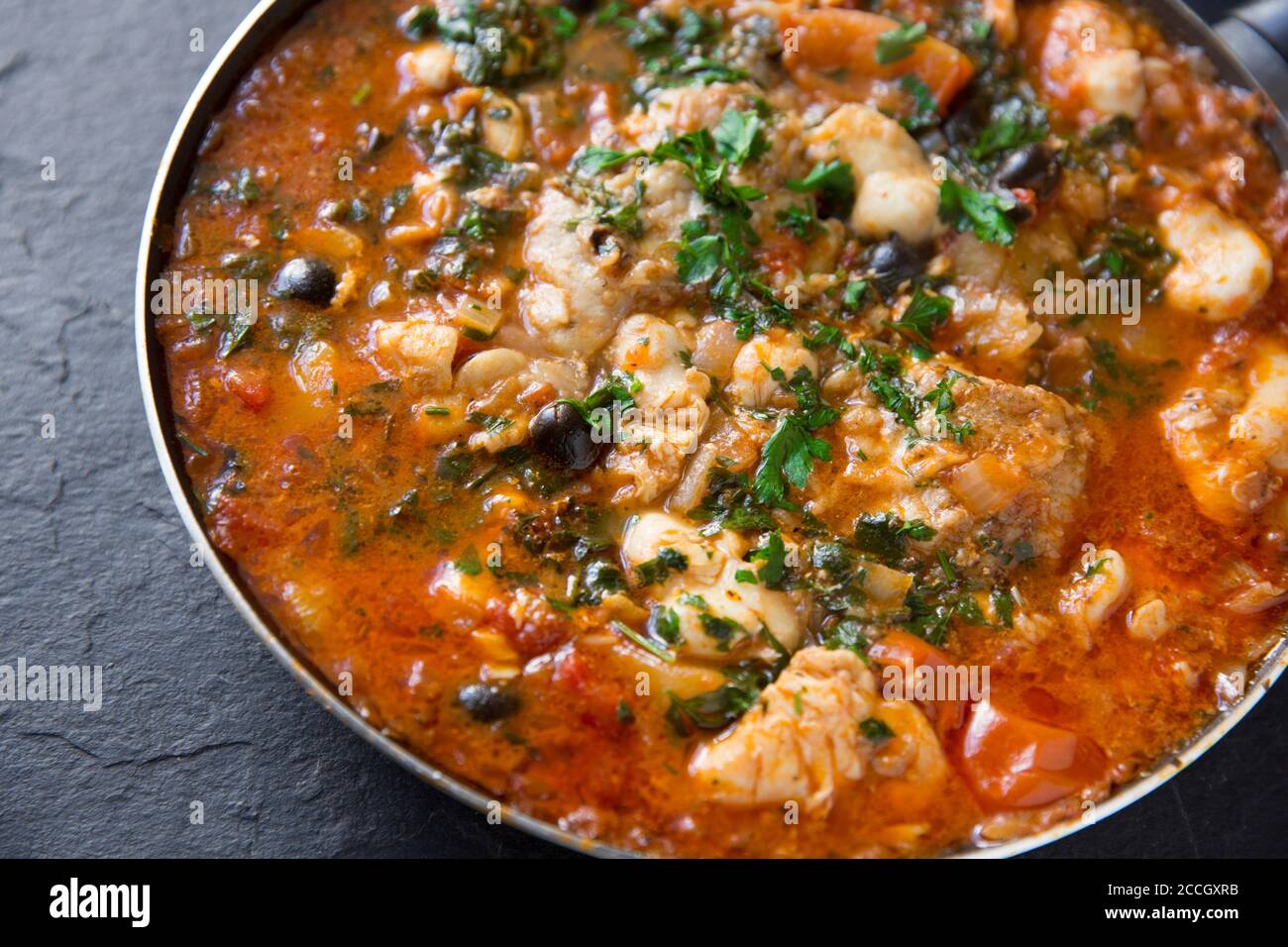 Un ragoût de poisson fait maison avec des joues de monkfish et des joues de rayon cuites dans une sauce tomate avec des pommes de terre bouillies, des olives noires et garnies de Banque D'Images