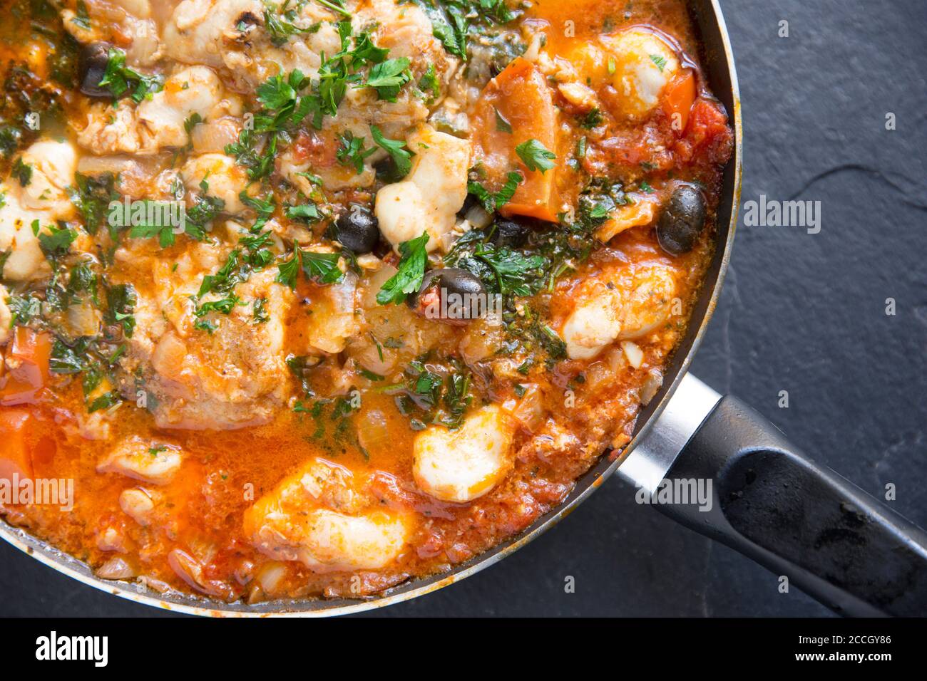Un ragoût de poisson fait maison avec des joues de monkfish et des joues de rayon cuites dans une sauce tomate avec des pommes de terre bouillies, des olives noires et garnies de Banque D'Images
