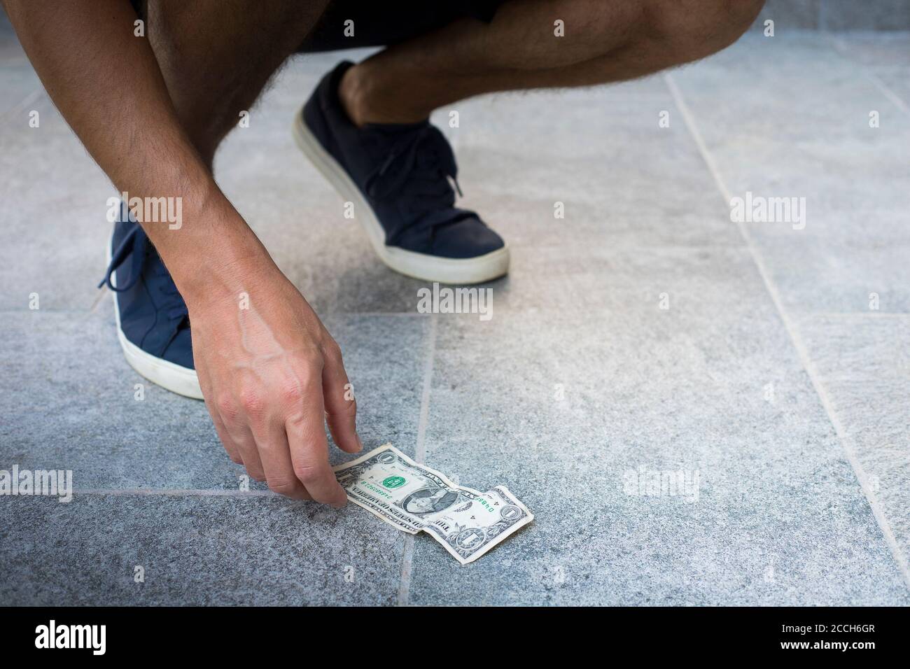Homme anonyme, décontracté habillé, avec des baskets bleues, prenant un billet d'un dollar du sol. Banque D'Images