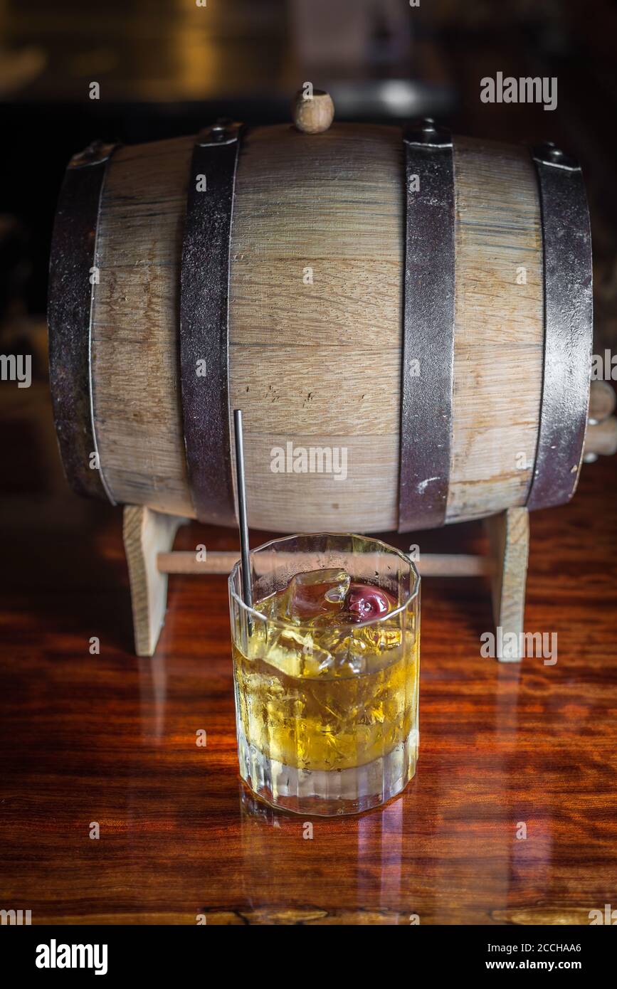 Ambiance de bar rustique avec un cocktail artisanal classique préparé avec du whisky bourbon et un tonneau assis sur le bar en bois. Banque D'Images
