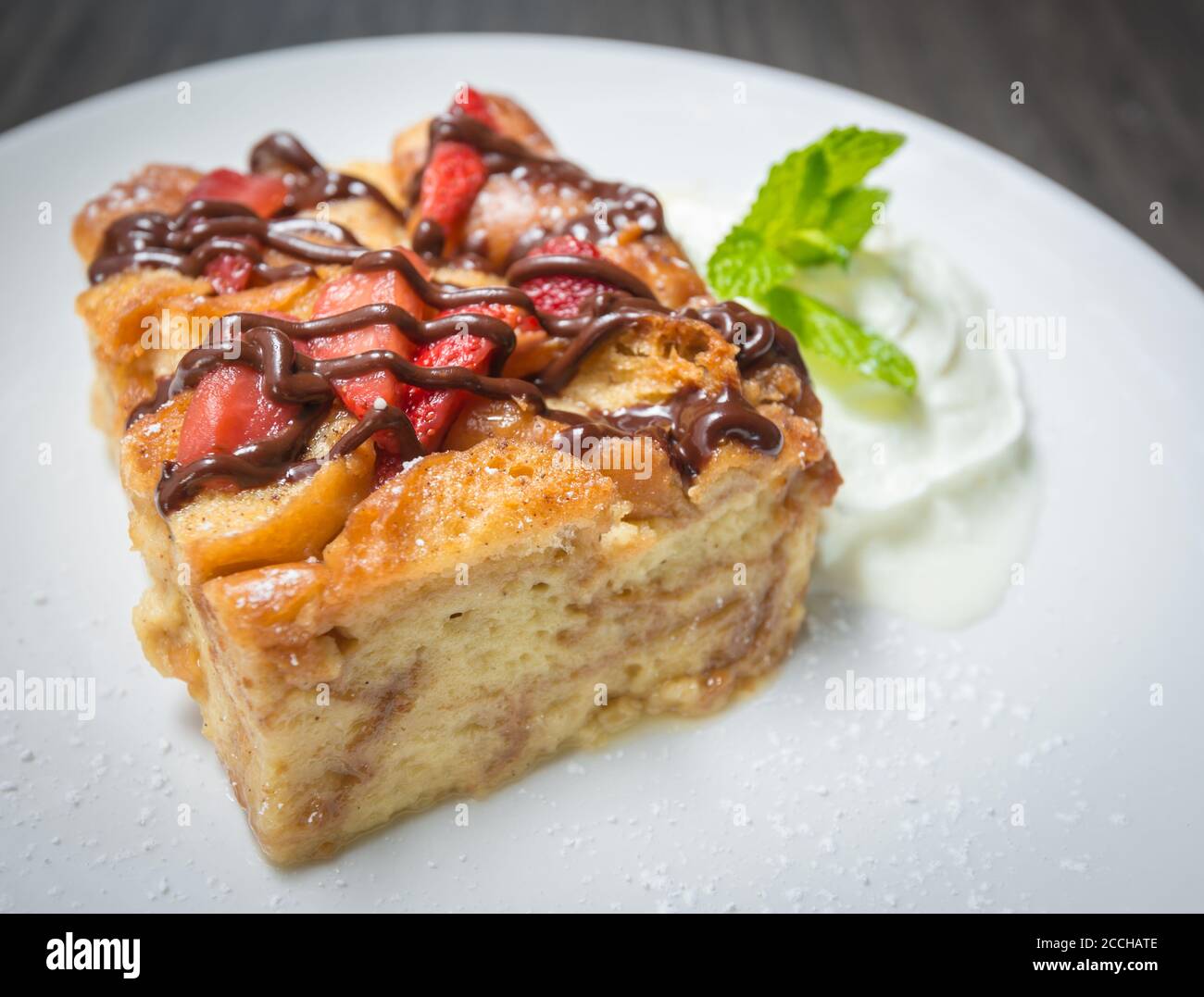 Une grande tranche de gâteau fait maison, recouverte de fraises fraîches et de chocolat, servi avec de la crème fouettée et de la menthe Banque D'Images