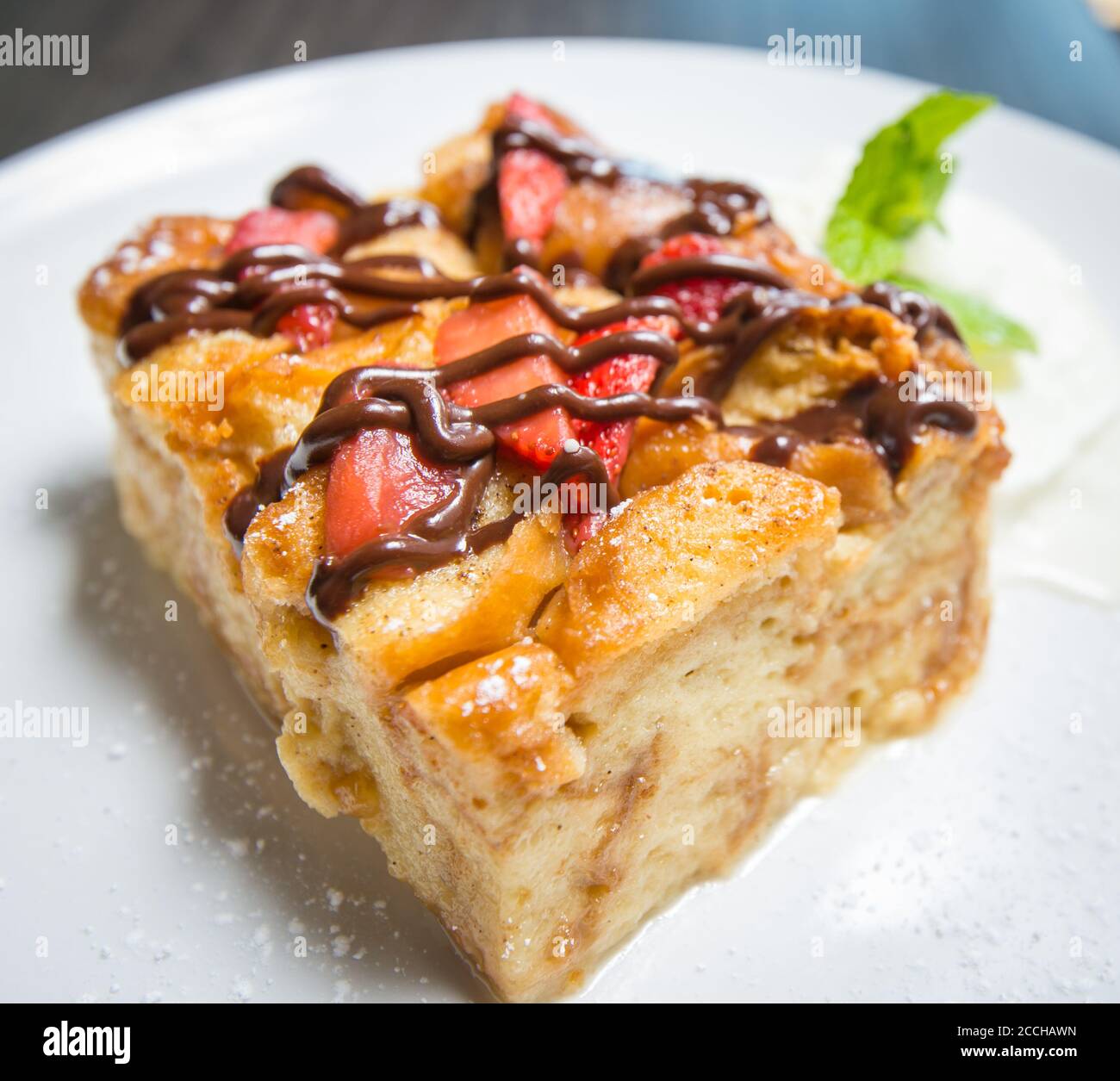 Une tranche de pudding au pain nappée de fraises et de sauce au chocolat, servie avec de la crème fouettée Banque D'Images