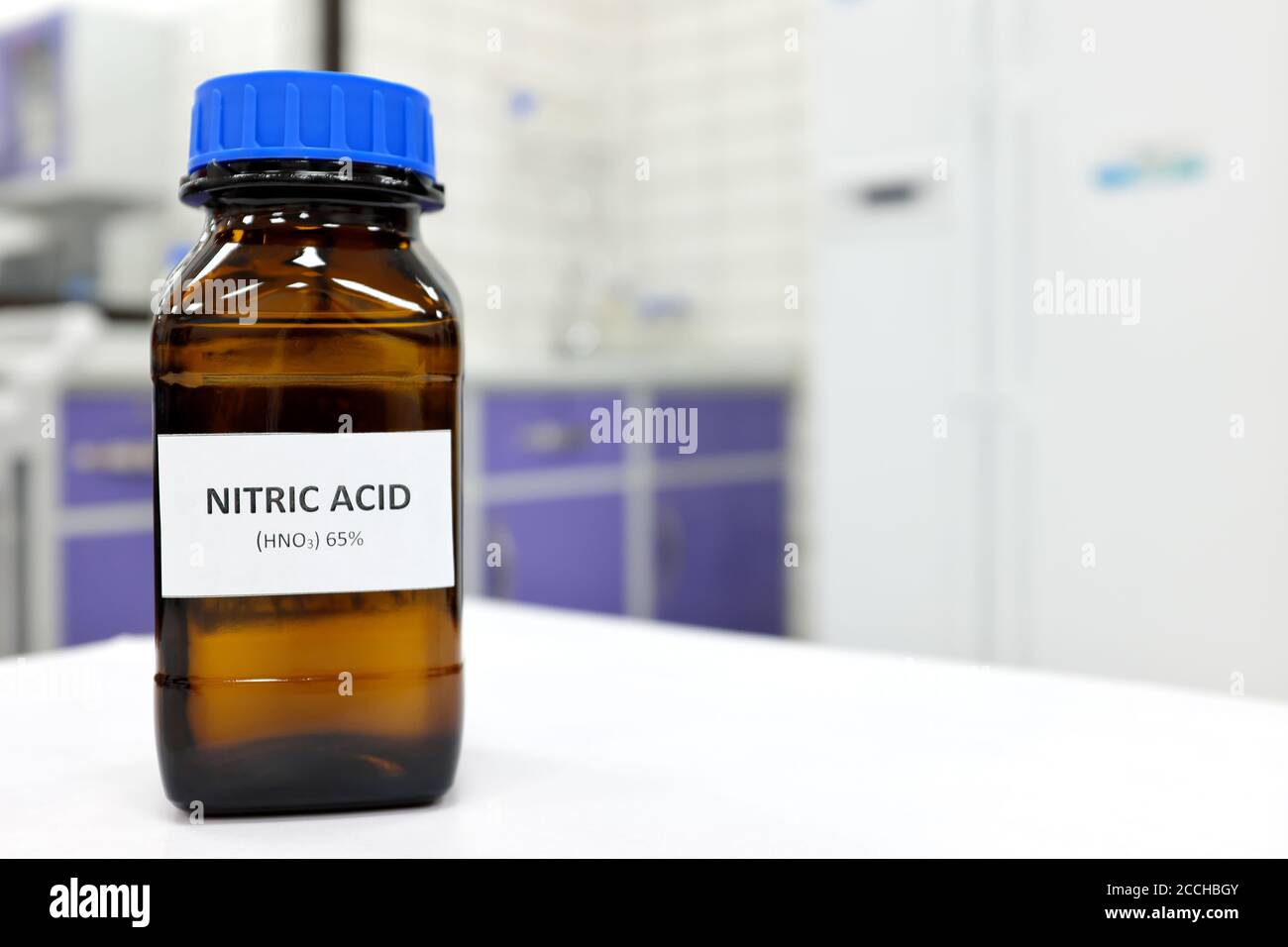 Concentration sélective d'une solution d'acide nitrique forte dans un flacon brun ambré. Fond de laboratoire blanc flou avec espace de copie. Banque D'Images