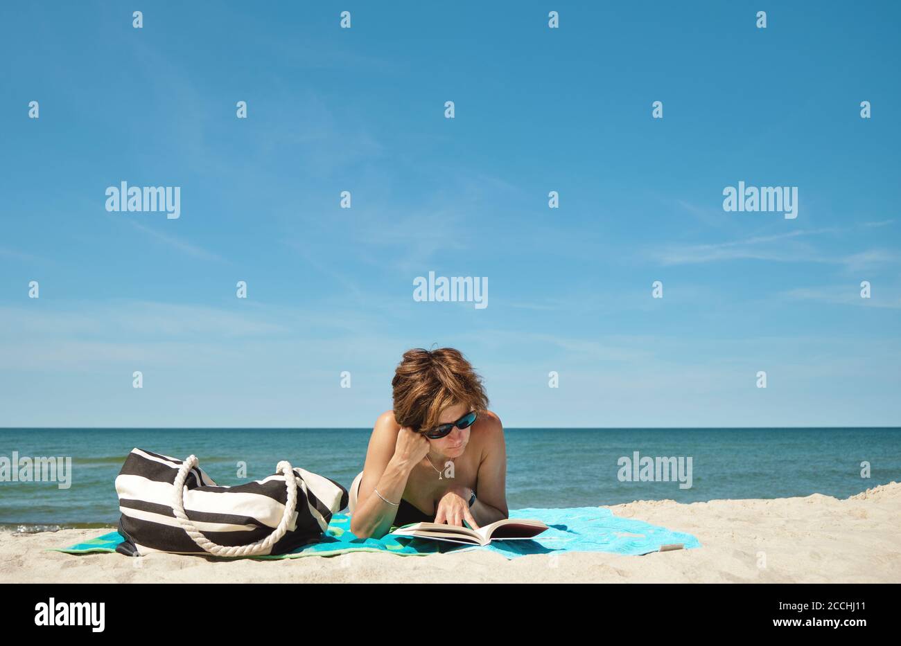 Belle femme d'âge moyen caucasien dans le bikini allongé sur le plage et lecture d'un livre les jours d'été Banque D'Images