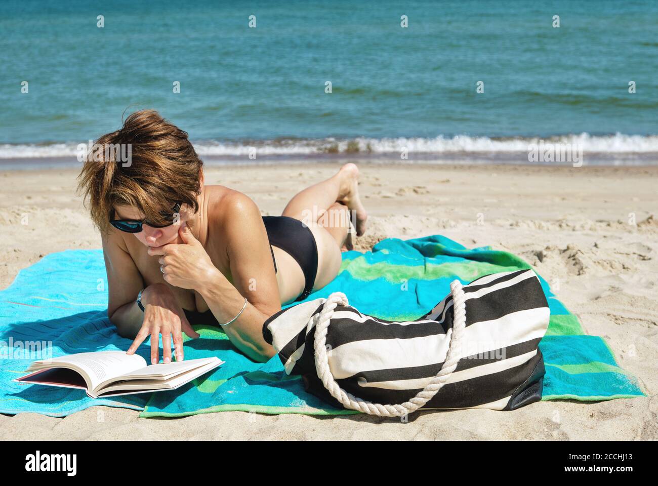 Femme caucasienne d'âge moyen dans le bikini allongé sur la plage lecture d'un livre les beaux jours d'été Banque D'Images