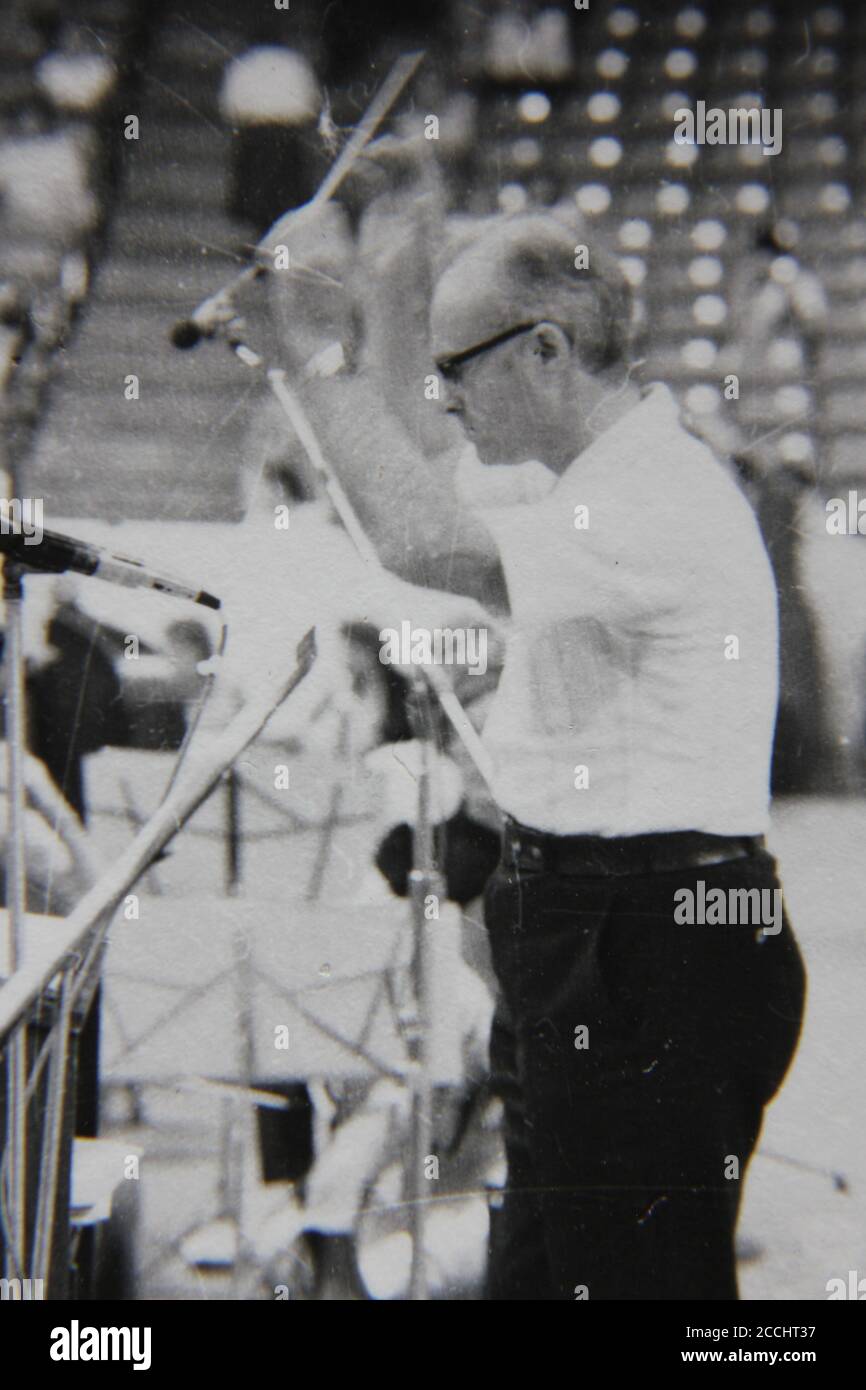 Belle photographie en noir et blanc vintage des années 1970 d'un chef de musique dirigeant un orchestre. Banque D'Images