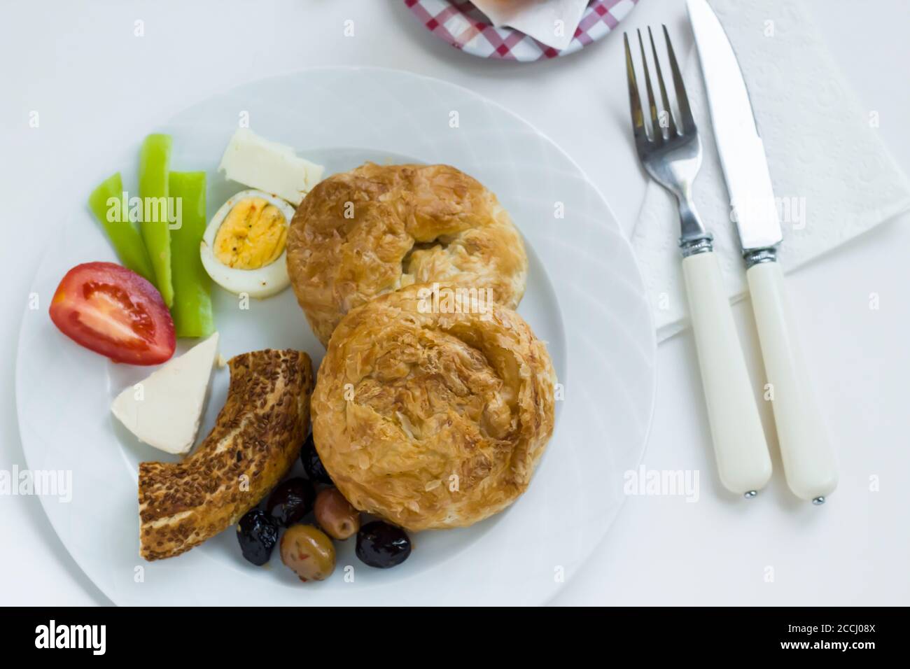 Pâtisserie traditionnelle turque « Boyoz » dans une assiette avec bagel au sésame, œuf, olives et tomates en tranches, petit déjeuner en blanc avec thé Banque D'Images