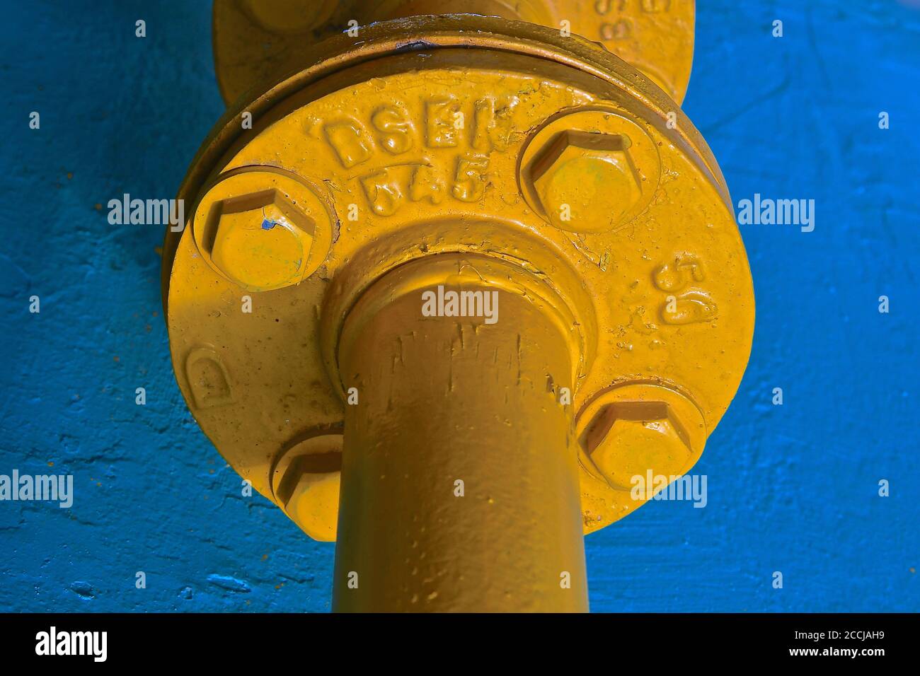 Vue rapprochée d'un grand raccord de tuyau en fonte industrielle jaune sur fond de pierre bleue. Banque D'Images