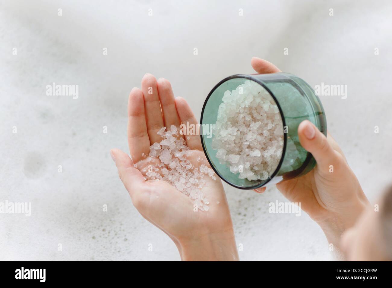 Gros plan de sel de bain de mer dans les mains de femme contre le fond de bain de mousse. Banque D'Images