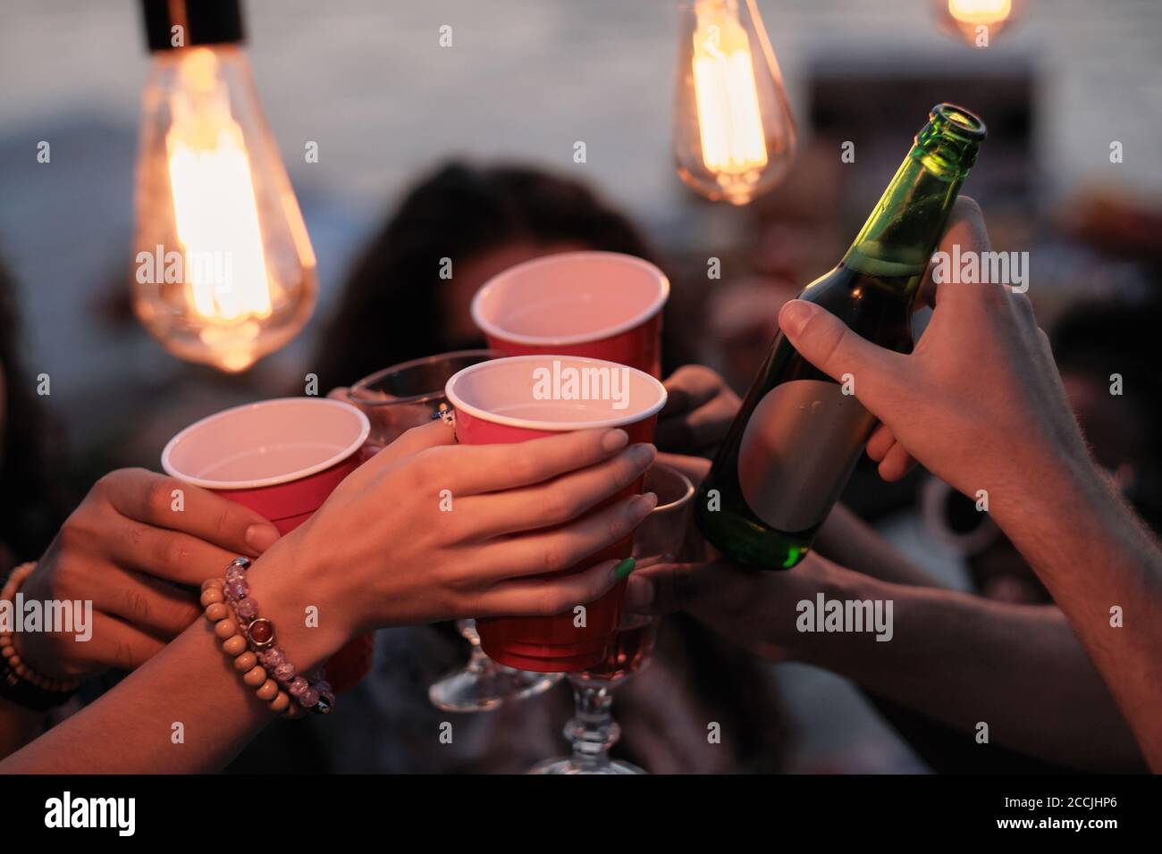 Gros plan des jeunes portant des verres avec de la bière et du toaster avec eux pendant une fête Banque D'Images