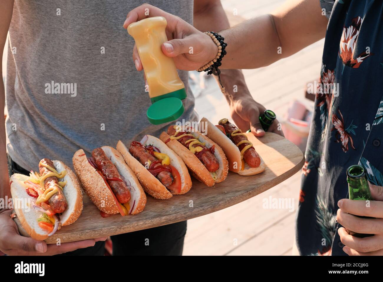 Gros plan des jeunes ajoutant de la sauce sur les hot dogs ils préparation de la nourriture pour la fête à l'extérieur Banque D'Images